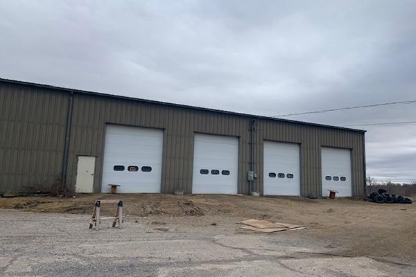 Large beige warehouse with 4 white overhead doors on paved lot.